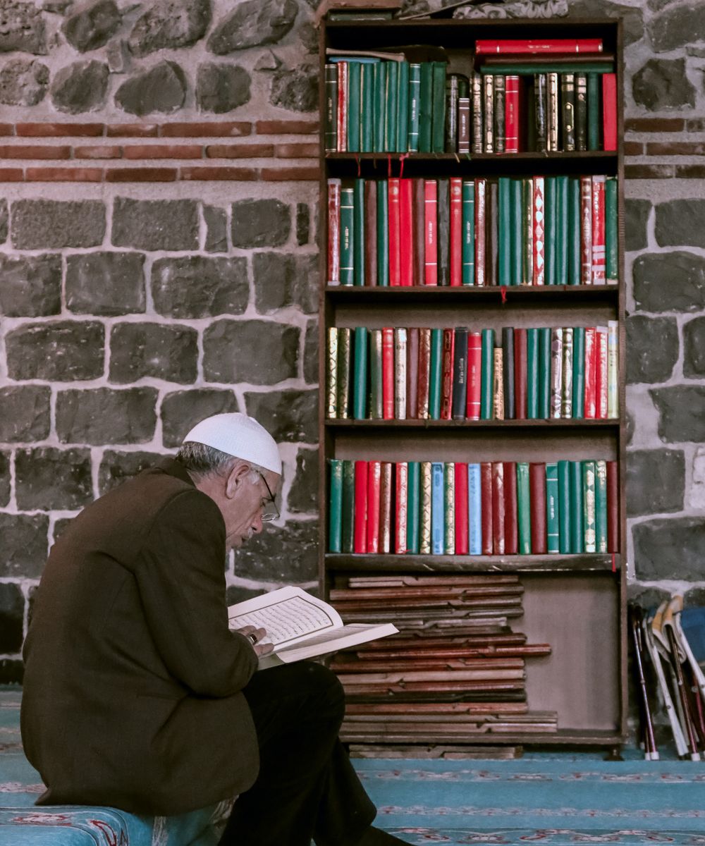 عالم مسلم يطالع كتباً قديمة بين رفوف مكتبة هادئة
